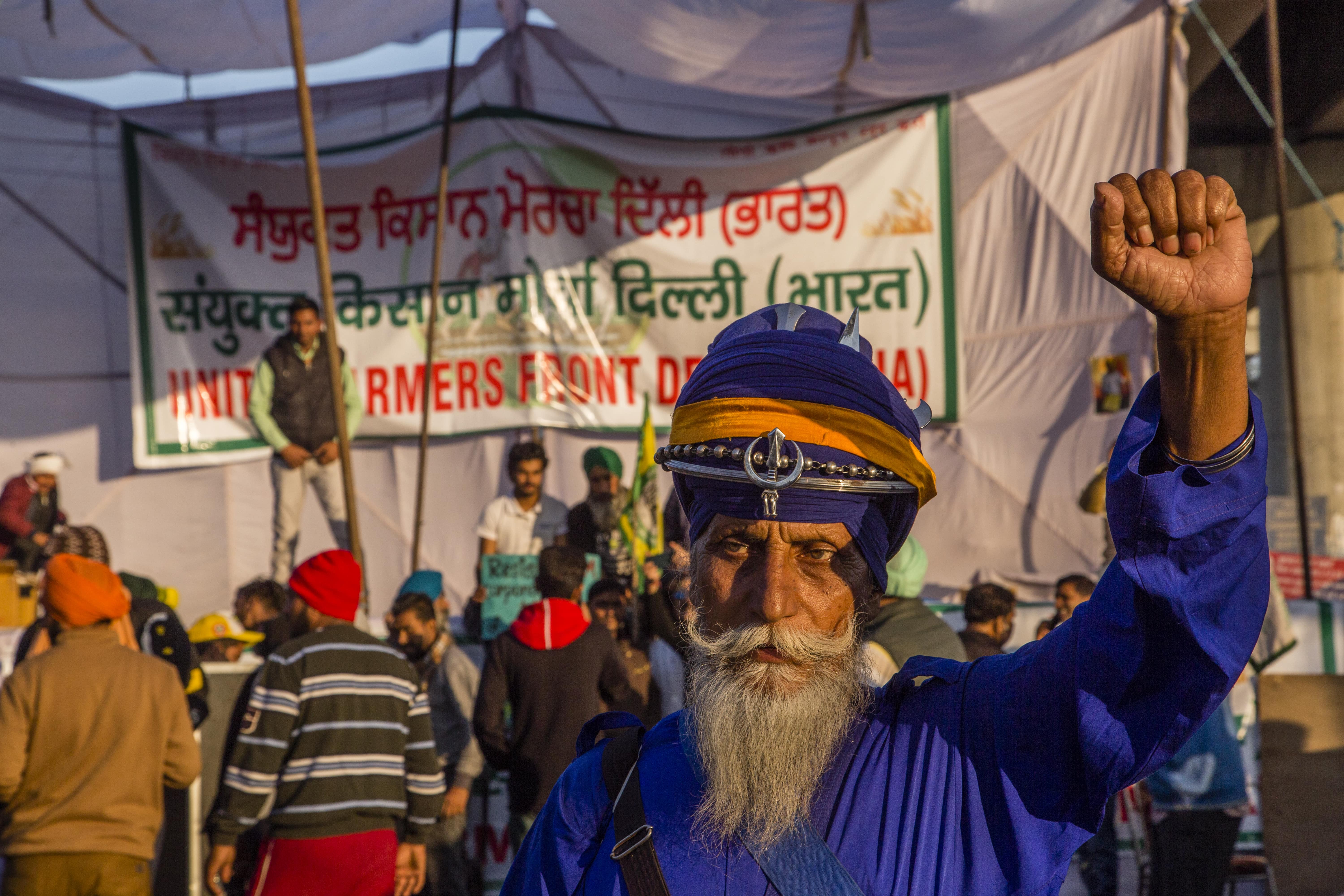 A bearded man dressed all in blue raises up his fist at a political rally for Indian farmers.