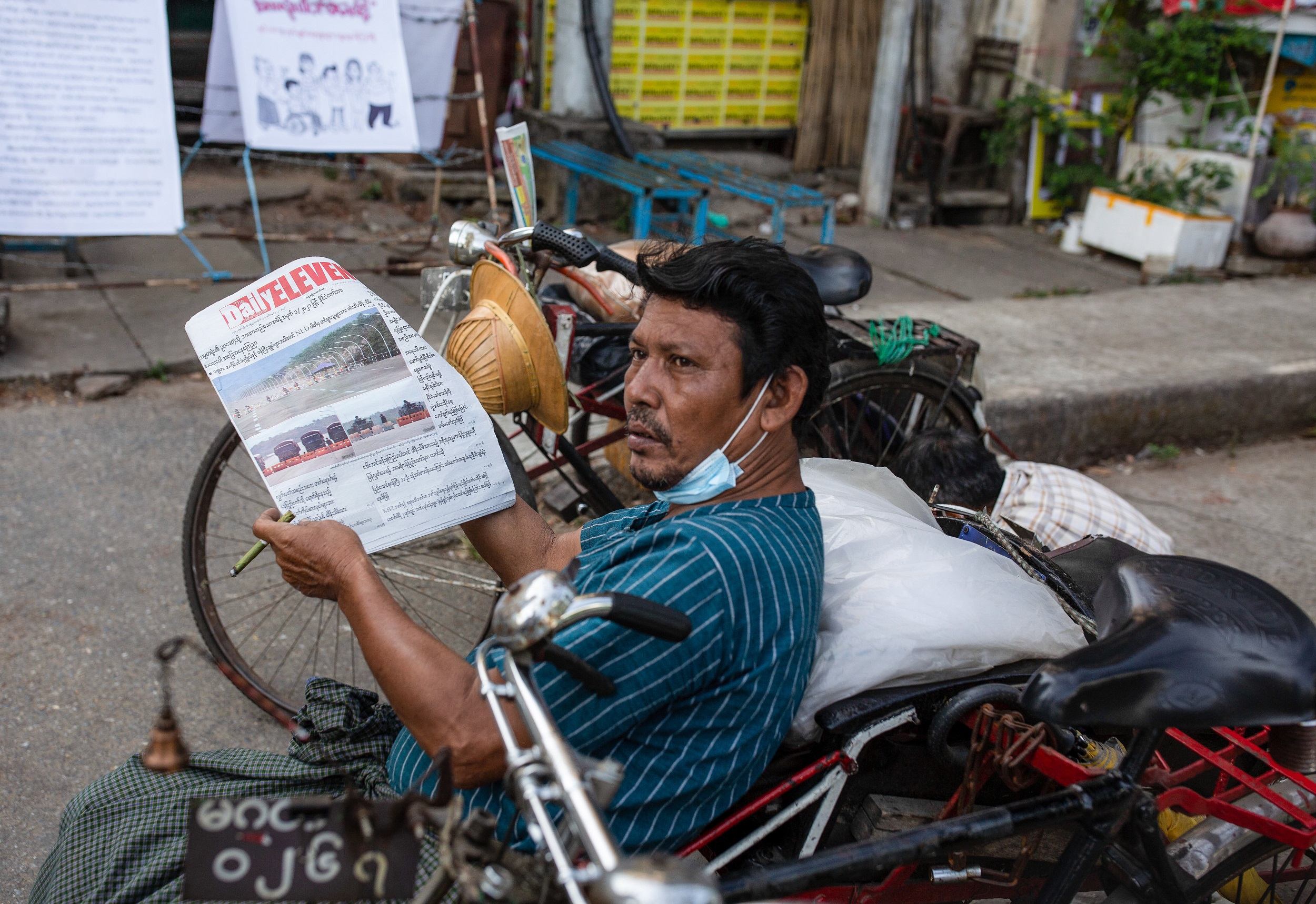 A picture of a man reading a newspaper, leaning on a motorcycle.