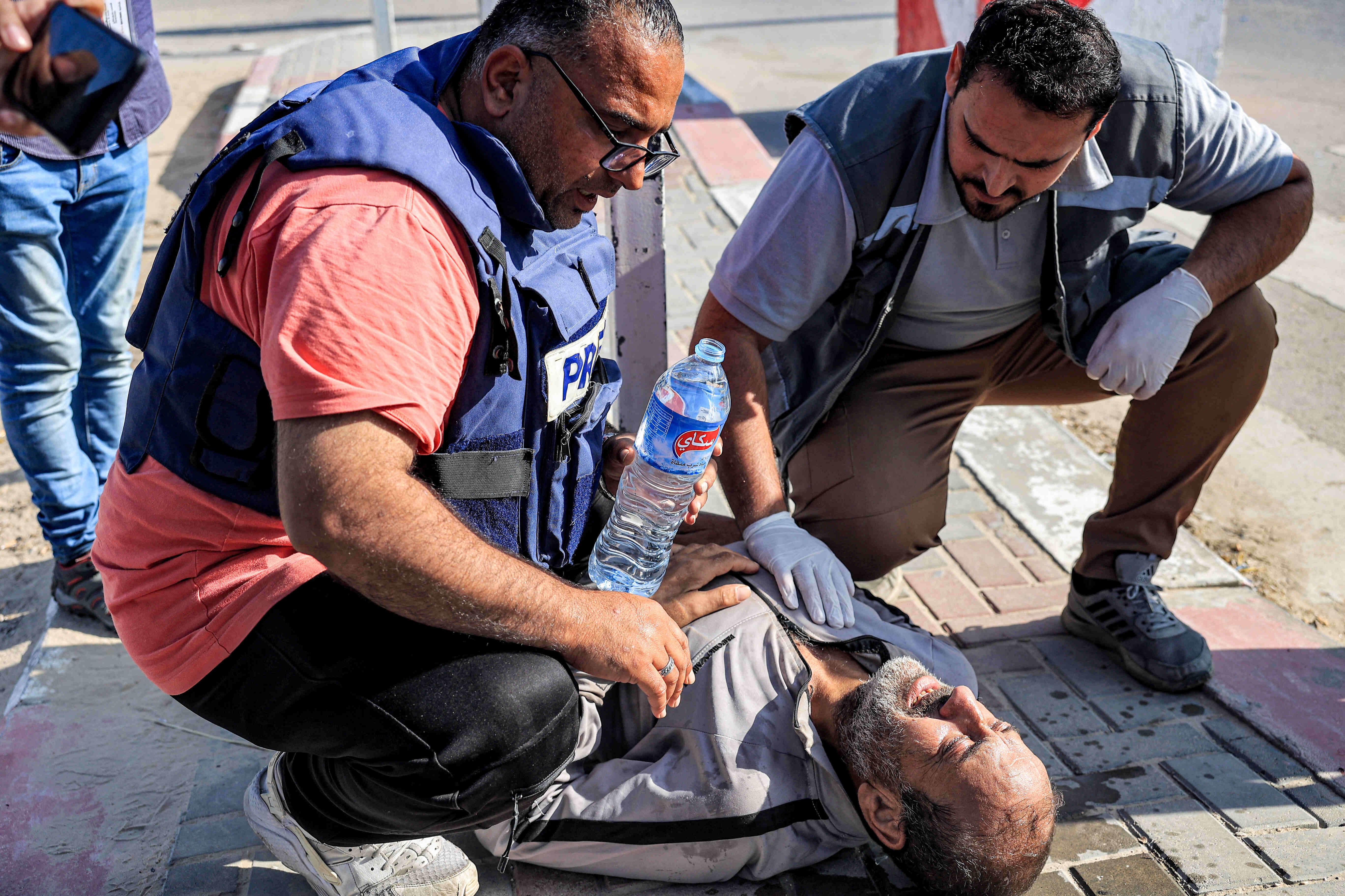 A journalist and paramedic assist one of the Palestinian workers who were stranded in Israel since the October 7 attacks after he collapsed upon arriving at the Rafah border crossing with Egypt after crossing into the Gaza Strip at the Kerem Shalom commercial border crossing with Israel in the south of the Palestinian enclave on November 3, 2023. (Photo by SAID KHATIB / AFP)