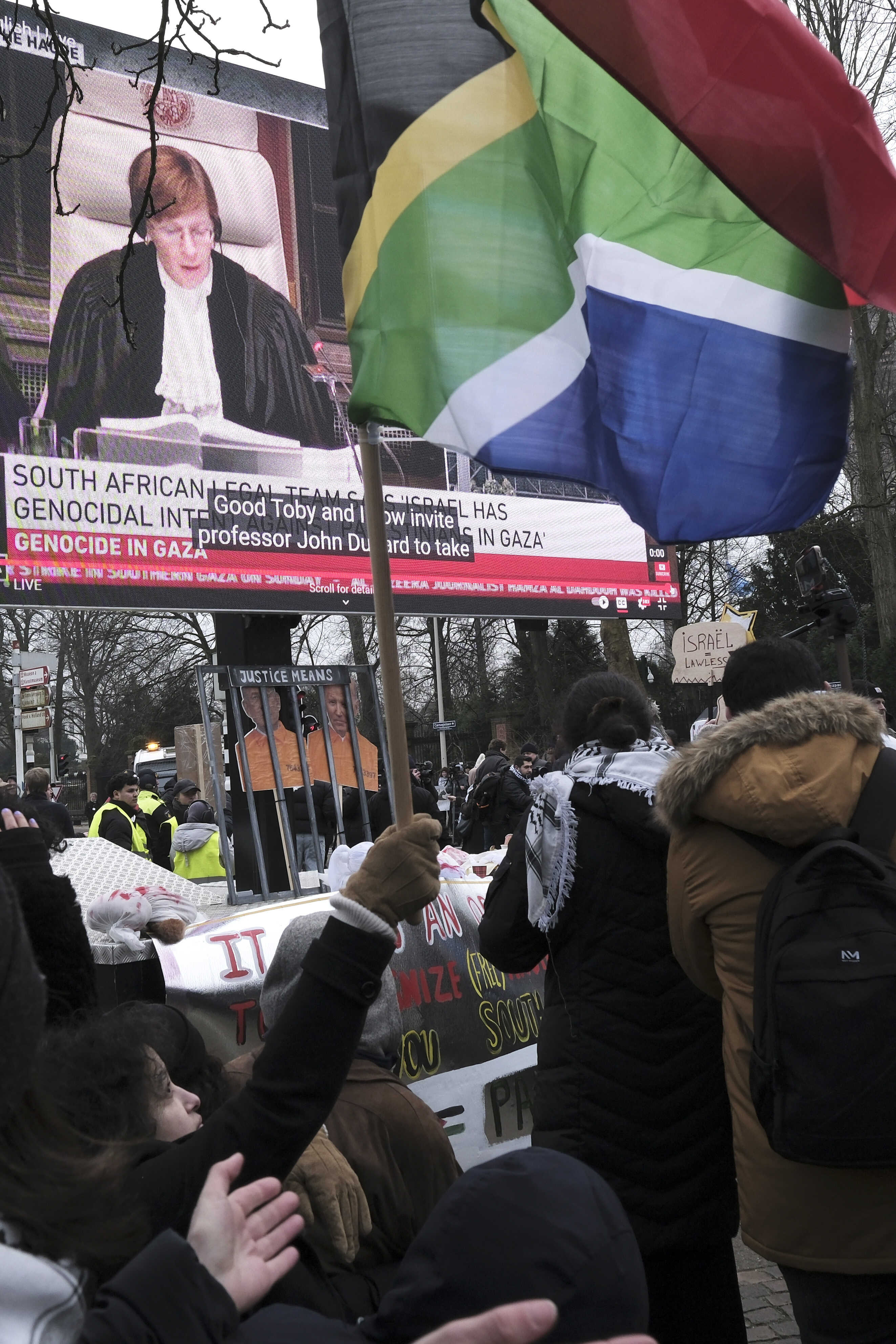Israel Palestinians World Court Genocide Defense A Protestor waves a South African flag in front of a giant video screen projecting a hearing during a demonstration outside the International Court of Justice in The Hague, Netherlands, Thursday, Jan. 11, 2024. The United Nations' top court opens hearings Thursday into South Africa's allegation that Israel's war with Hamas amounts to genocide against Palestinians, a claim that Israel strongly denies. (AP Photo/Patrick Post)