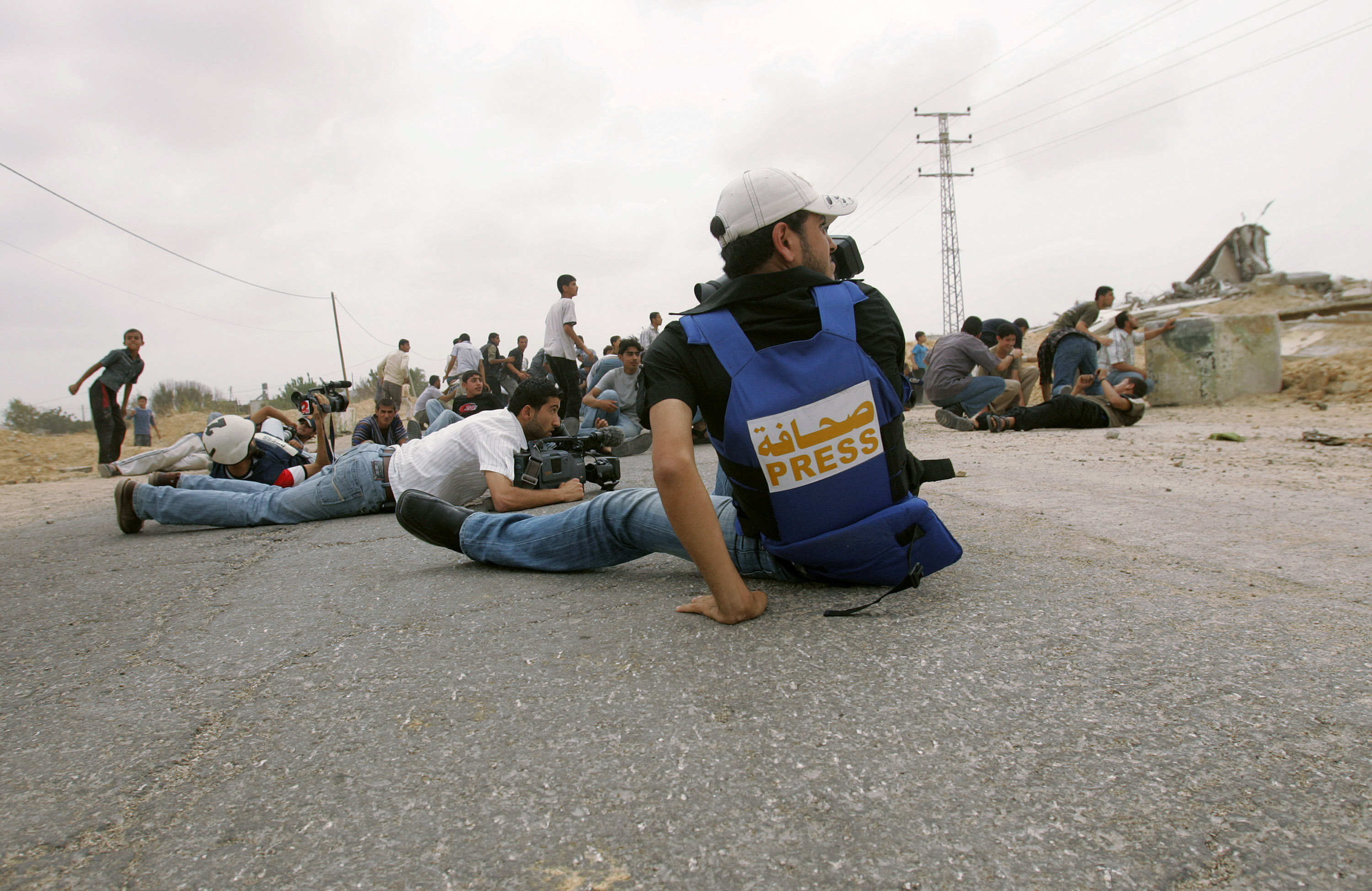 A picture of Palestinian journalists laying on their stomachs as Israeli snipers fire passes by them.