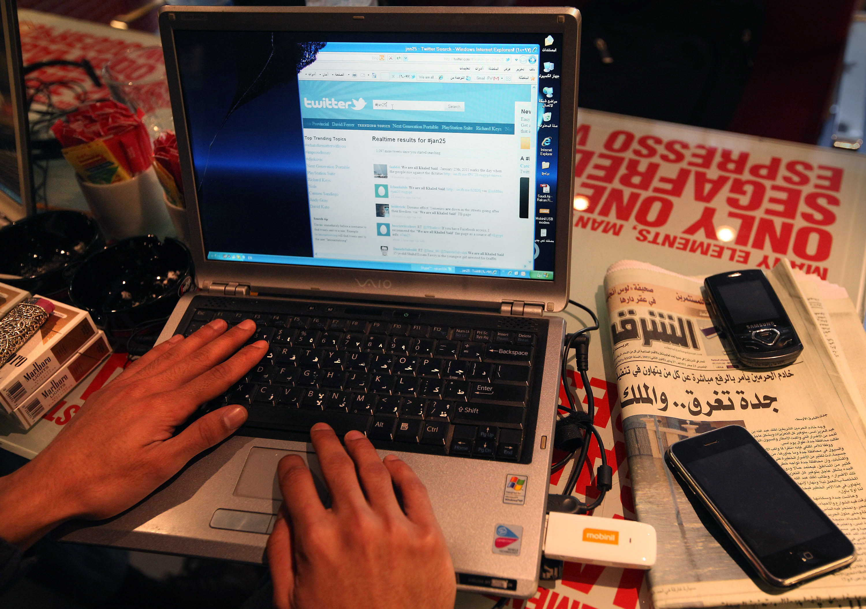 A picture of an open laptop with someone typing on it and a newspaper in arabic.
