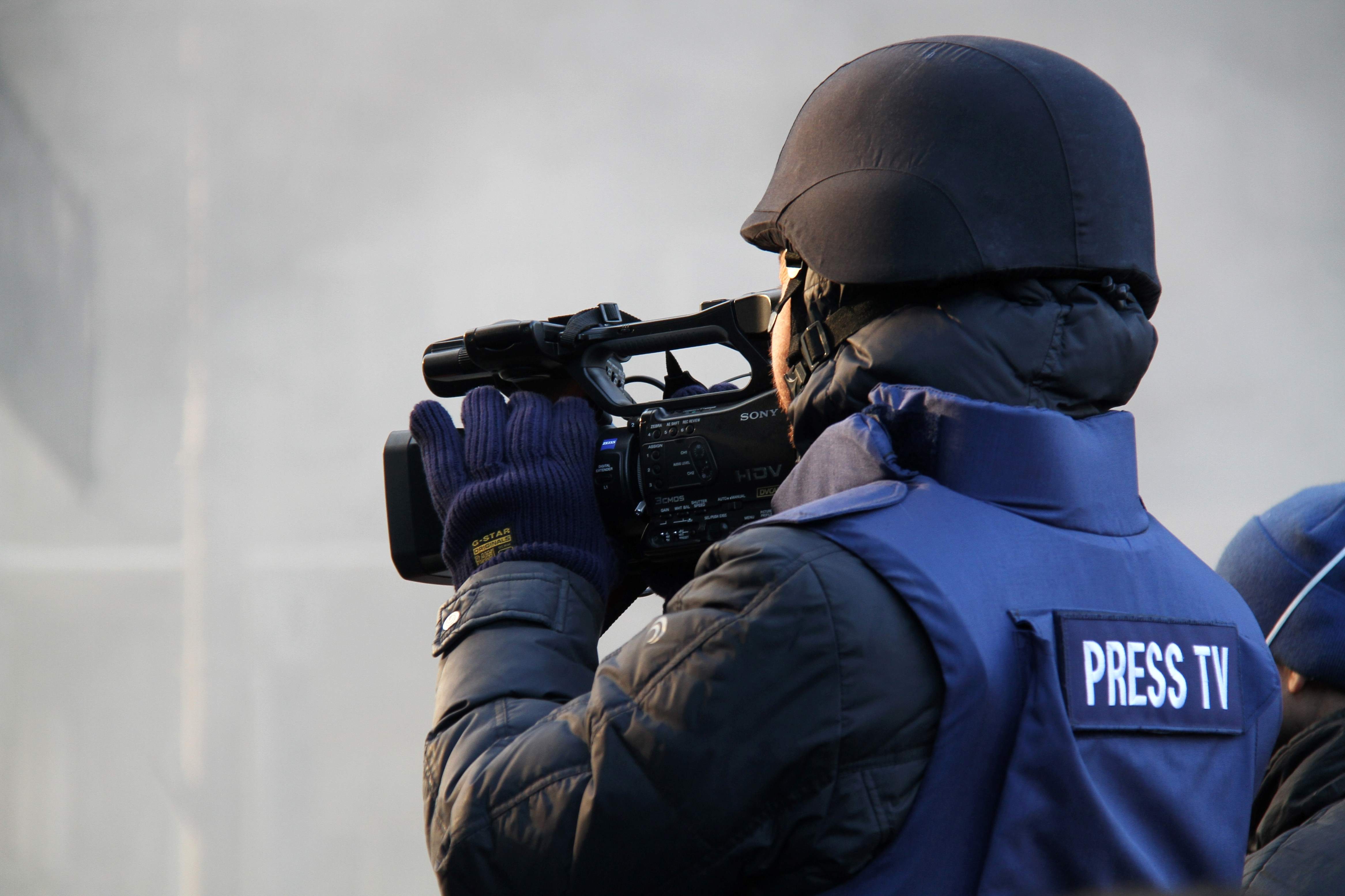 Journalist holding video camera wearing a blue helmet and a vest
