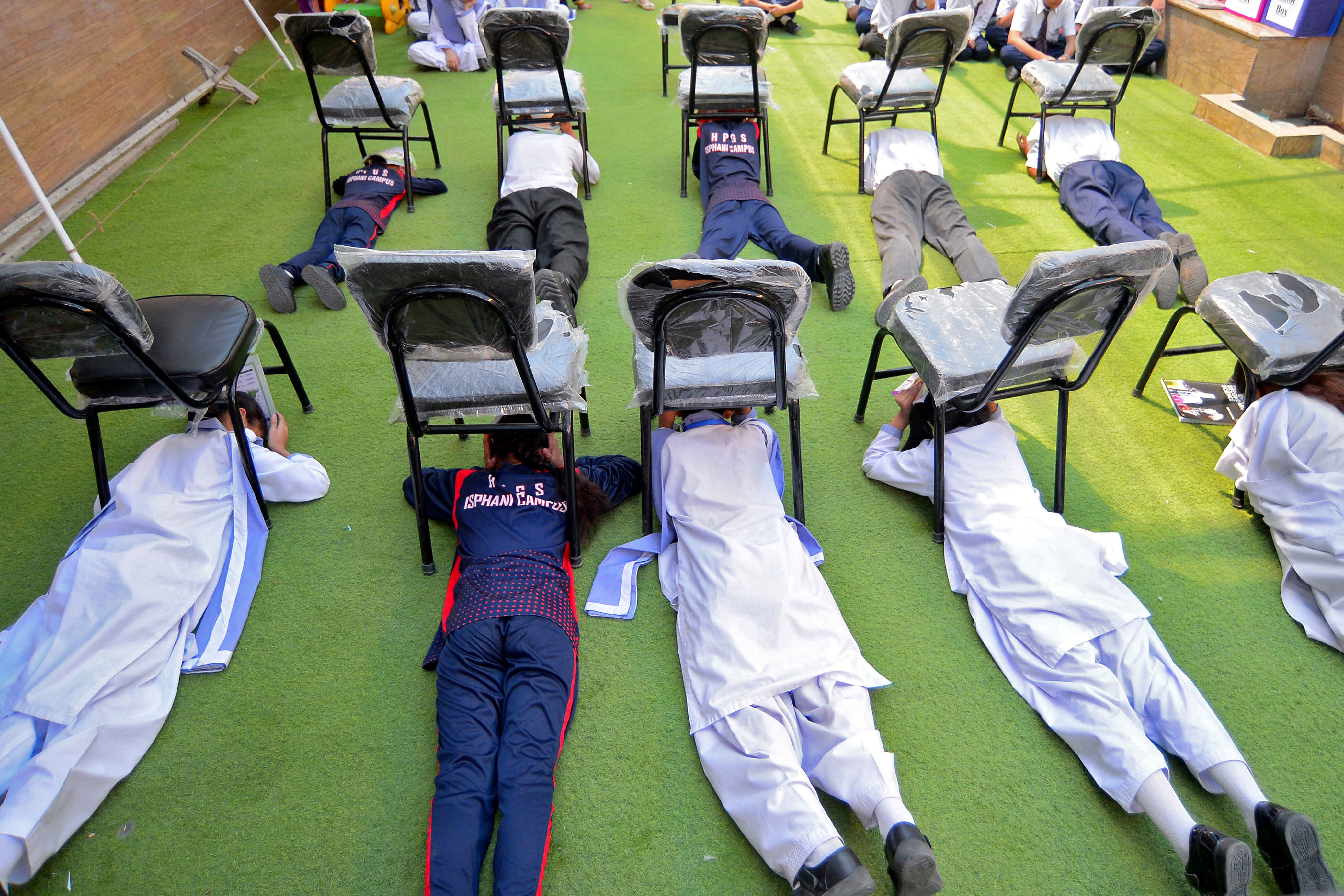Students use chairs to cover their heads inside a classroom at a school during a mock drill for handling war situations, in Karachi Friday, 9th May 2025