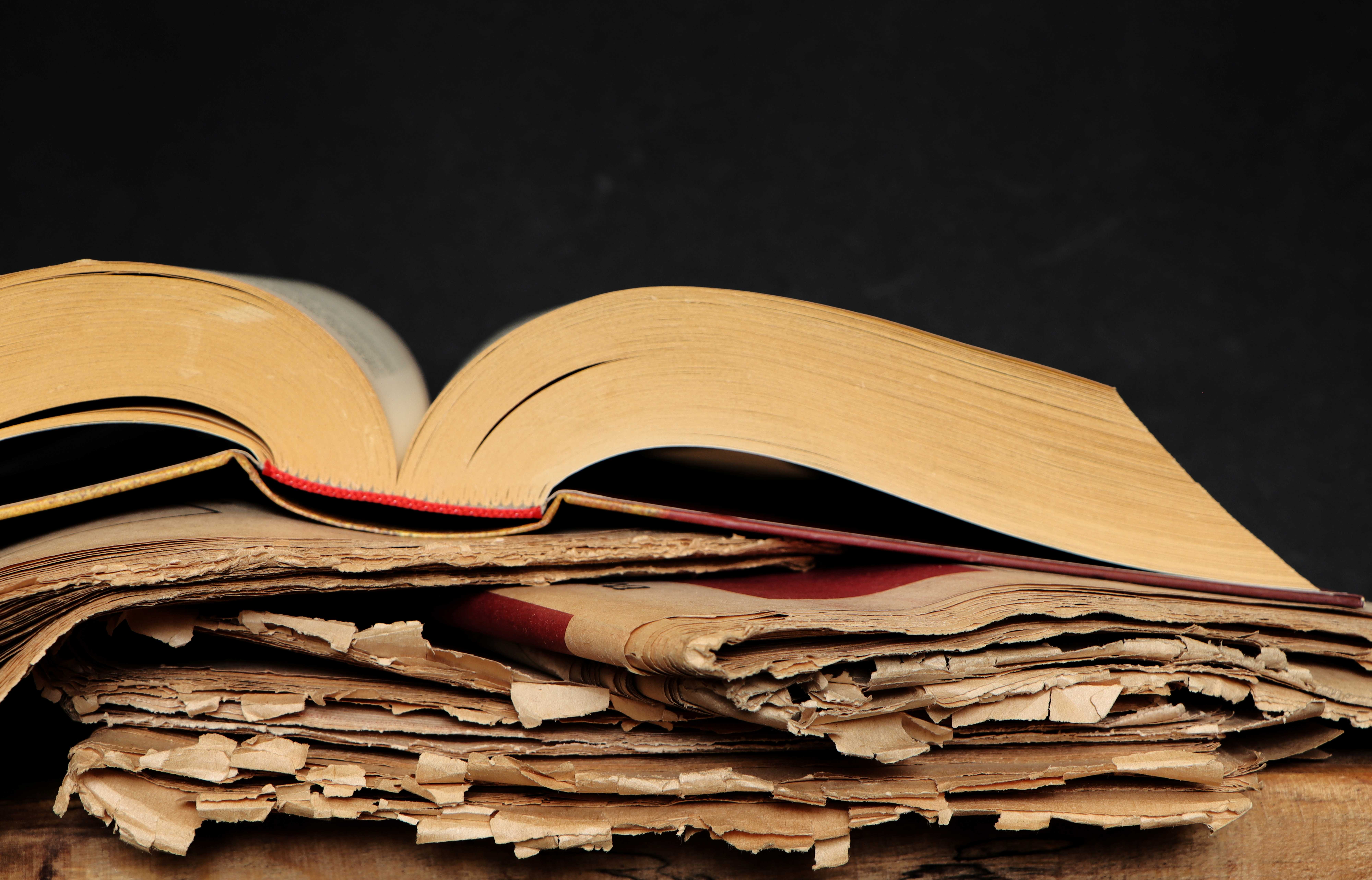 Old book open and stacked over some old newspapers, implying journalism's role in history