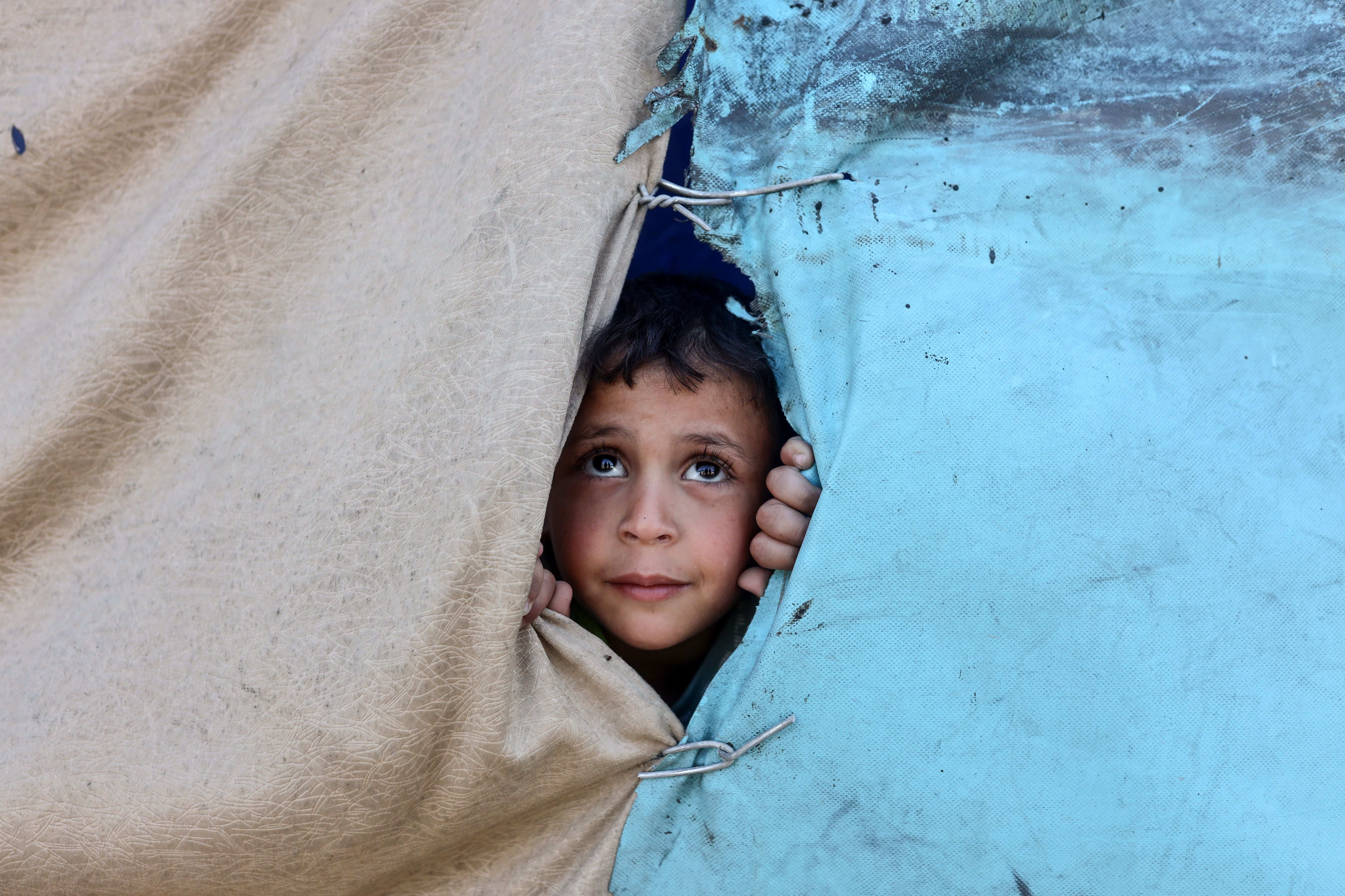 A boy looks out from a tent at a makeshift camp sheltering displaced Palestinians in the Zeitoun neighborhood of Gaza City. (Photo: Majdi Fathi. Gaza City, Palestine – Dec 2025)