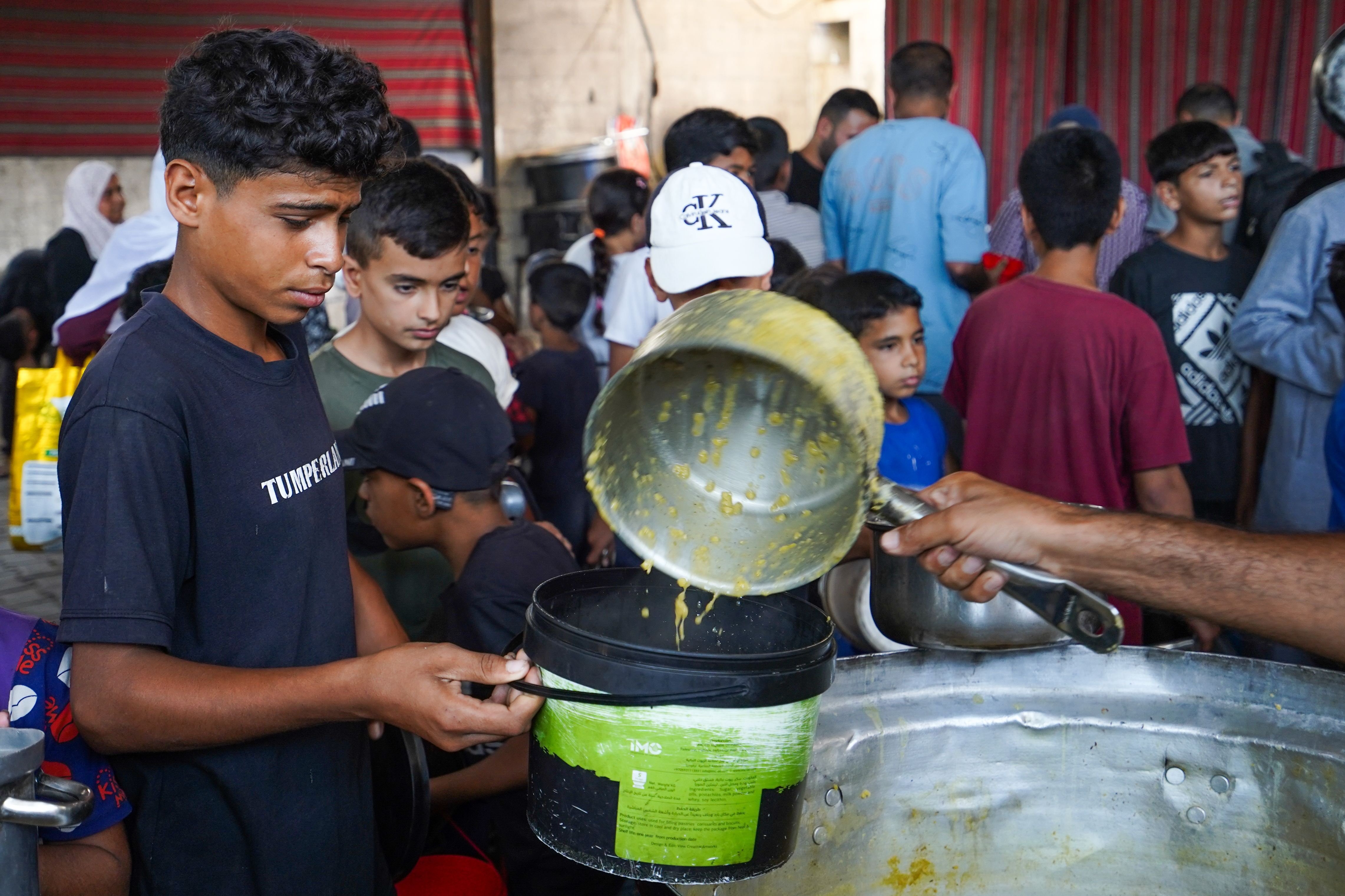 A displaced Palestinian child holds a container to receive a hot meal at a charity kitchen in the Al-Nuseirat camp, as severe food insecurity and restrictions on humanitarian aid continue to affect thousands of families across the Gaza Strip. (Photo: Ramzi Abu Amer/JNA via ZUMA Press Wire. Al-Nuseirat Camp, Palestine – Jul 2026)