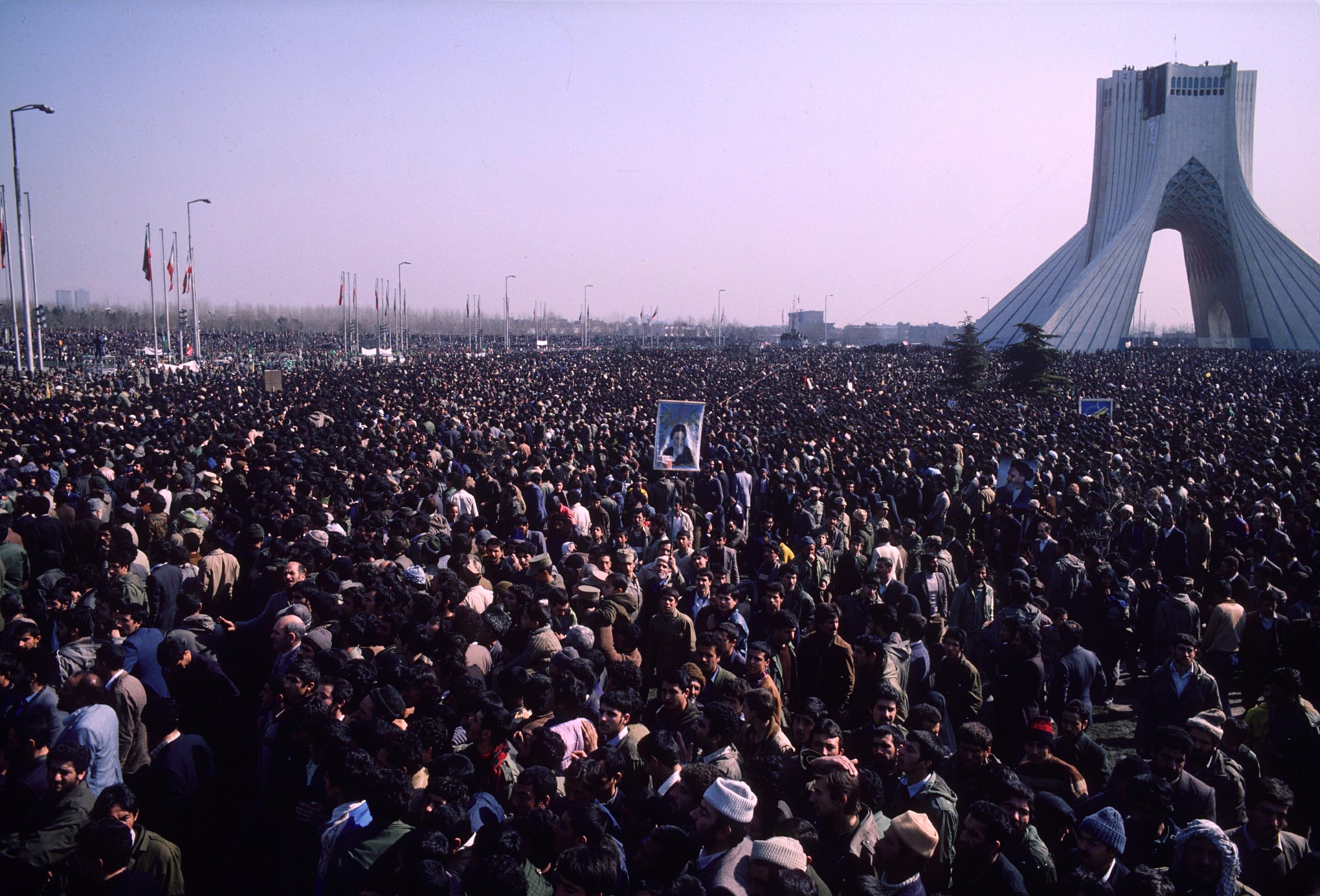 Massive crowds of demonstrators and supporters gather in Azadi Square, surrounding the iconic Shahyad Tower, to witness the historic return of Ayatollah Khomeini to Tehran. The event marks the end of Khomeini’s 15-year exile and signifies the definitive collapse of the Pahlavi monarchy, serving as a pivotal catalyst for the Islamic Revolution. This momentous assembly represents a sea change in Iran's political landscape, capturing the intense fervor and shifting power dynamics of the era.
