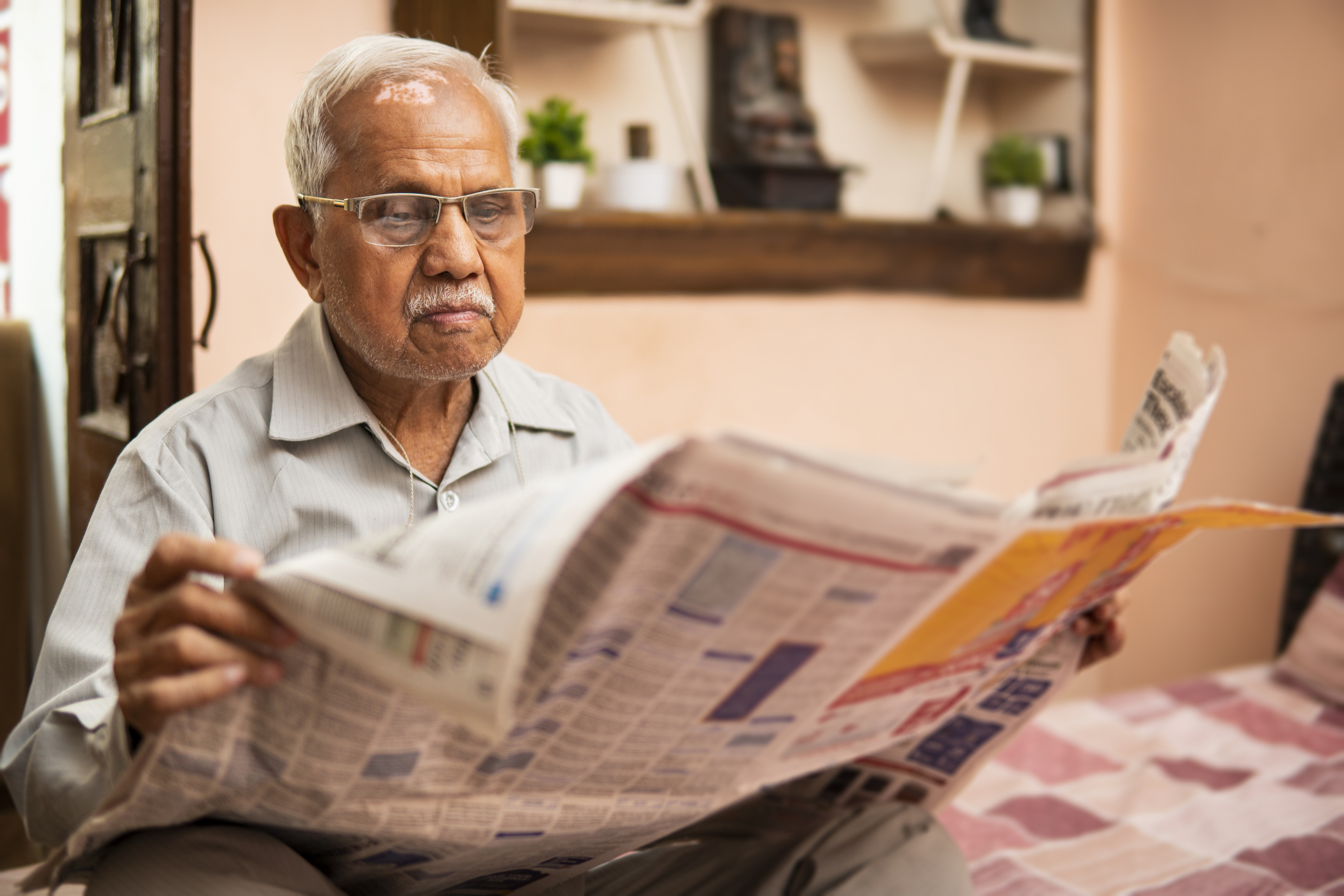 Senior Indian man reading newspaper in leisure time at home. - stock photo Senior Indian man sitting relaxed on the bed and reading a newspaper in the morning at home.