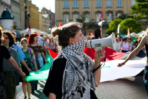Woman wearing a Kufiyeh  in a protest holding a megaphone