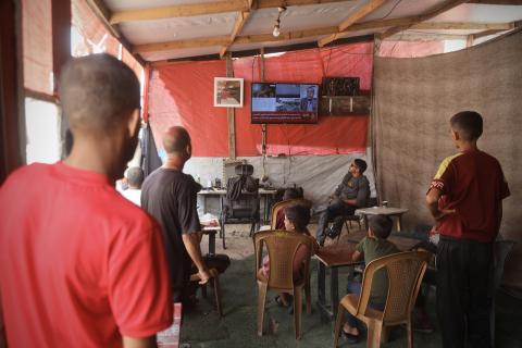 Palestinians watching the news on TV screen inside a makeshift tent in Gaza