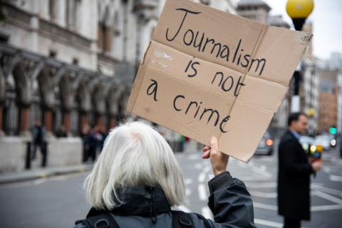 Back of woman holding placard that reads: Journalism is not a crime