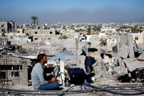 A Palestinian man smokes shisha as he looks at the houses destroyed in Israeli strikes during the war at the Khan Younis refugee camp, in the southern Gaza Strip, November 29, 2023. REUTERS/Mohammed Salem