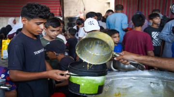 A displaced Palestinian child holds a container to receive a hot meal at a charity kitchen in the Al-Nuseirat camp, as severe food insecurity and restrictions on humanitarian aid continue to affect thousands of families across the Gaza Strip. (Photo: Ramzi Abu Amer/JNA via ZUMA Press Wire. Al-Nuseirat Camp, Palestine – Jul 2026)